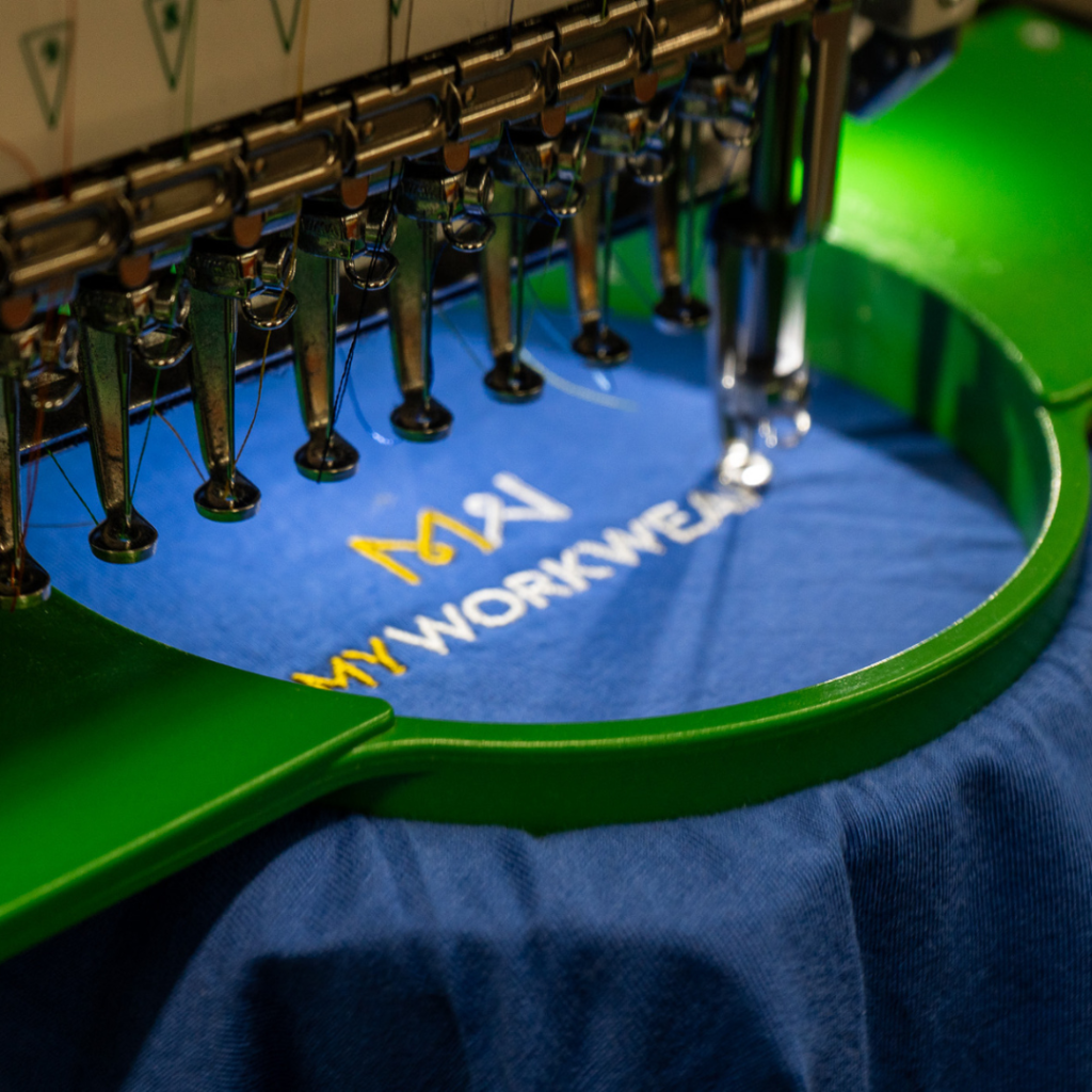 Embroidery machine, embroiding the MyWorkwear logo onto a blue t-shirt.