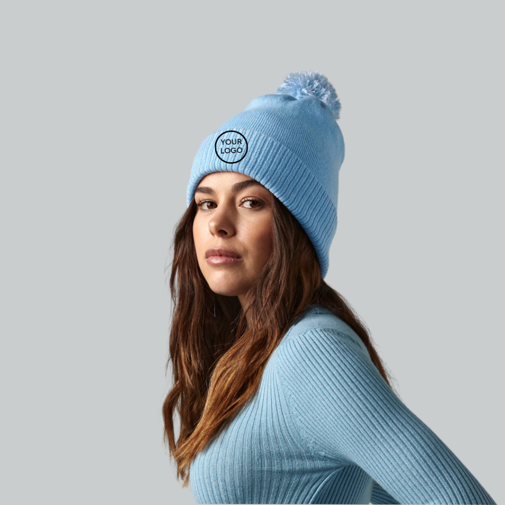 Woman wearing a light blue knitted, long sleeve top with a matching light blue beanie, that has a bobble.
